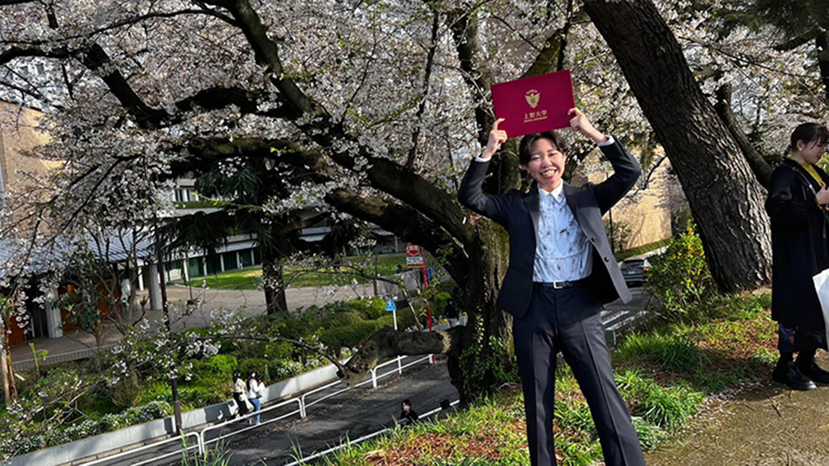 卒業式　桜の木の下で卒業証書を掲げる女性